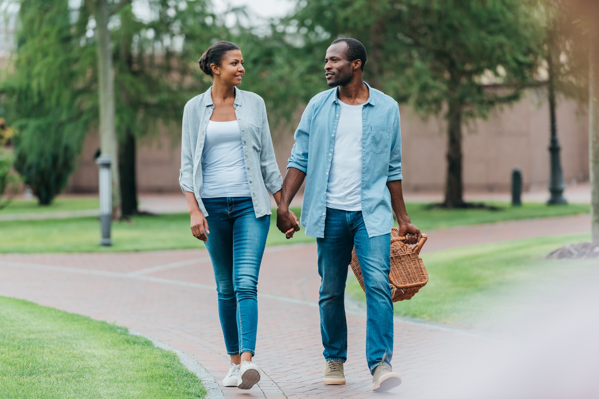 african american couple with picnic basket holding hands while walking in park