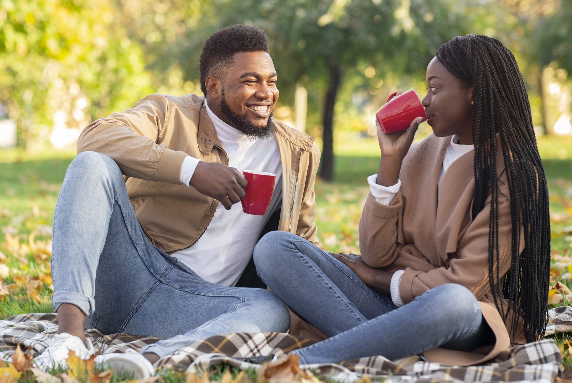 Afro couple dating in autumn park, having picnic and drinking tea